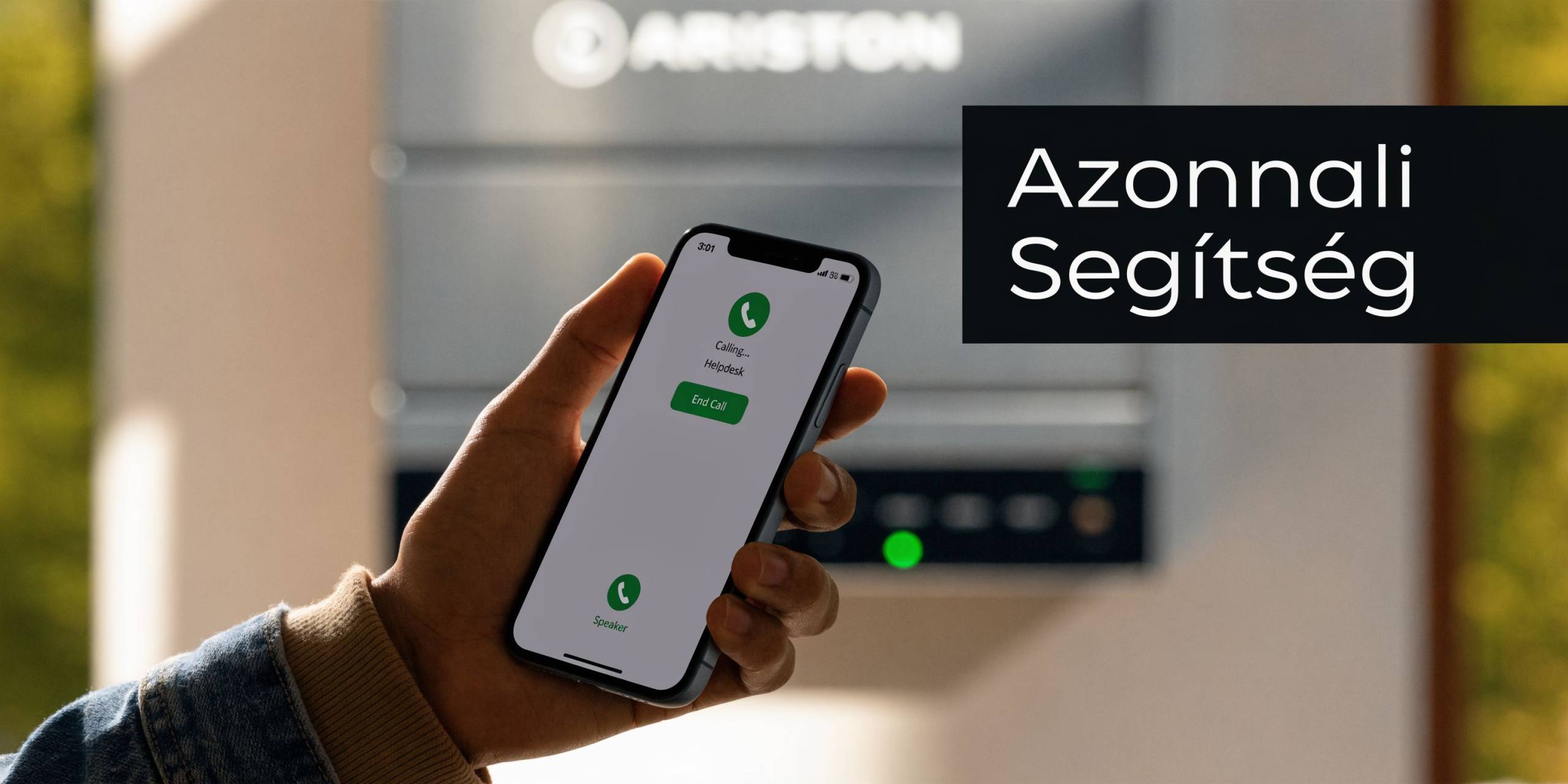 Valaki egy okostelefonon hívja az Ariston ügyfélszolgálatát, miközben a háttérben egy modern Ariston kazán látható.